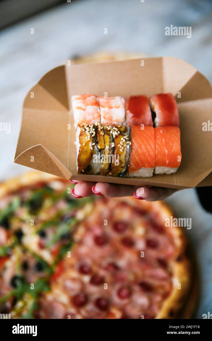 ensemble de sushi sur la boîte d'emballage dans la main sur fond de pizza. nourriture de rue Banque D'Images
