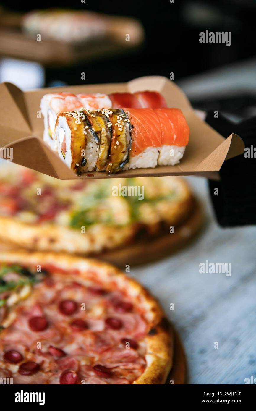 ensemble de sushi sur la boîte d'emballage dans la main sur fond de pizza. nourriture de rue Banque D'Images