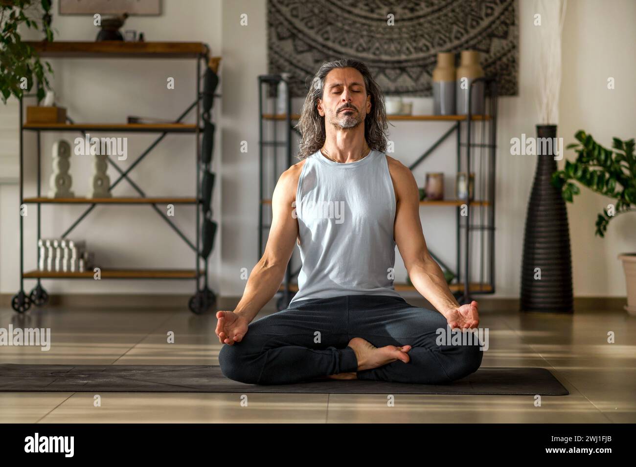 Homme adulte faisant Ardha Padmasana avec Gyan mudra pendant la méditation pleine conscience à la maison Banque D'Images
