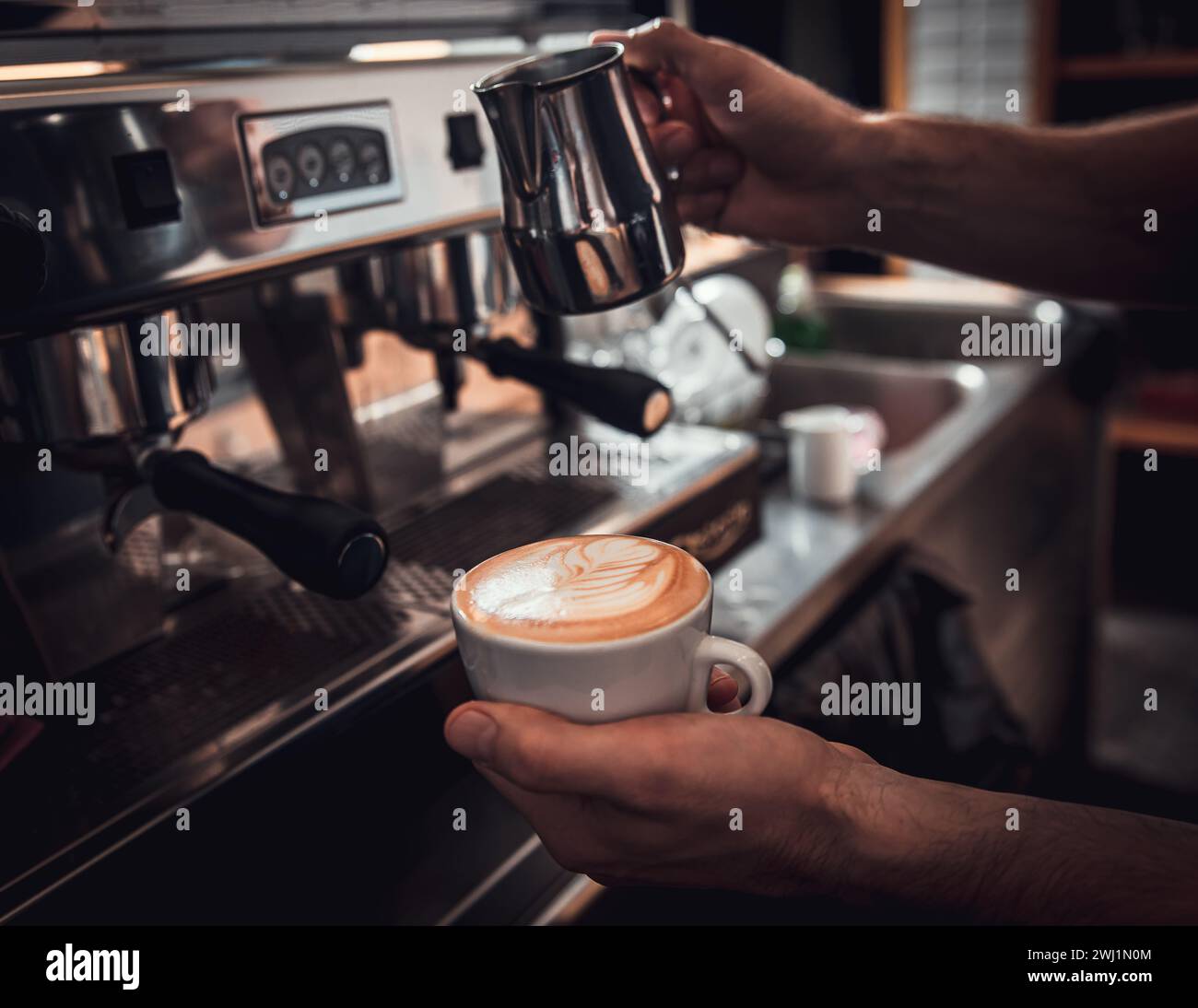 Gros plan des mains de barista préparant un cappuccino sur la machine à espresso pour le client dans le café. Banque D'Images