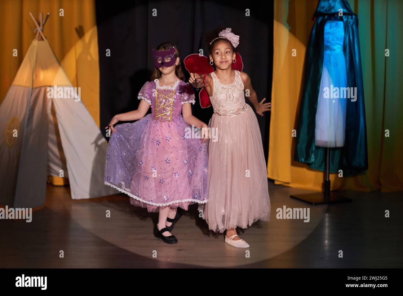 Portrait en pied de deux jeunes filles vêtues de costumes agissant sur scène dans un théâtre éclairé par un espace de copie de projecteur Banque D'Images