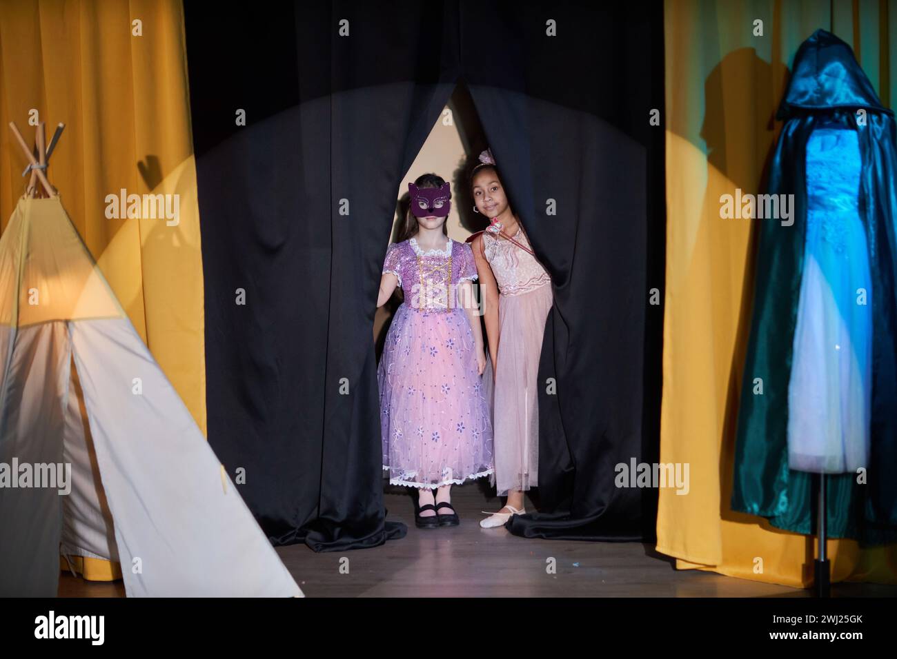 Portrait pleine longueur de deux petites filles entrant en scène dans le rideau d'ouverture de théâtre avec projecteur sur Banque D'Images