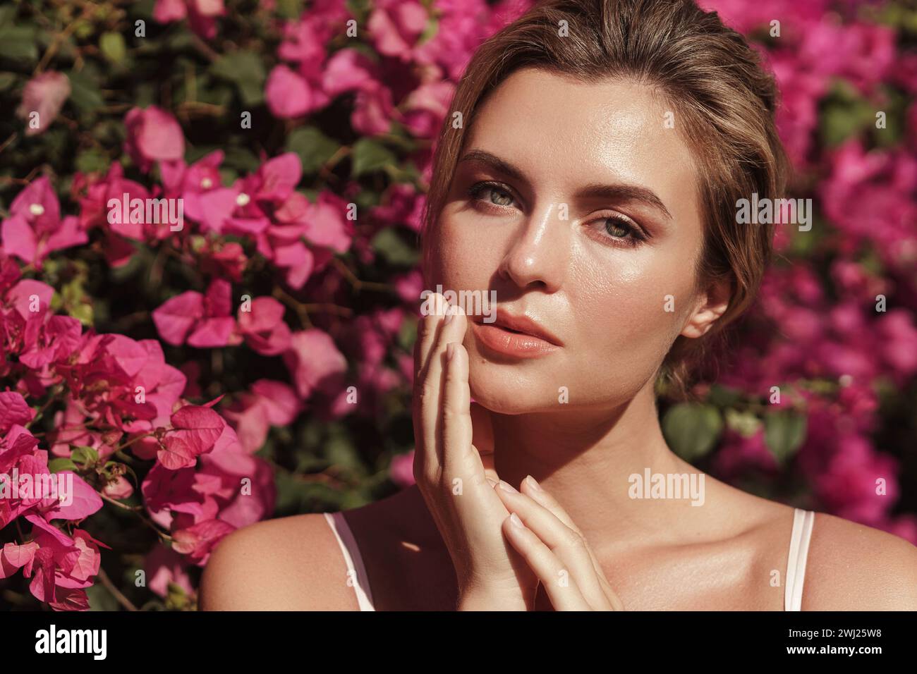 Belle femme blonde avec la peau lisse et le maquillage naturel, comme elle pose sur un fond d'un buisson avec des fleurs roses délicates Banque D'Images