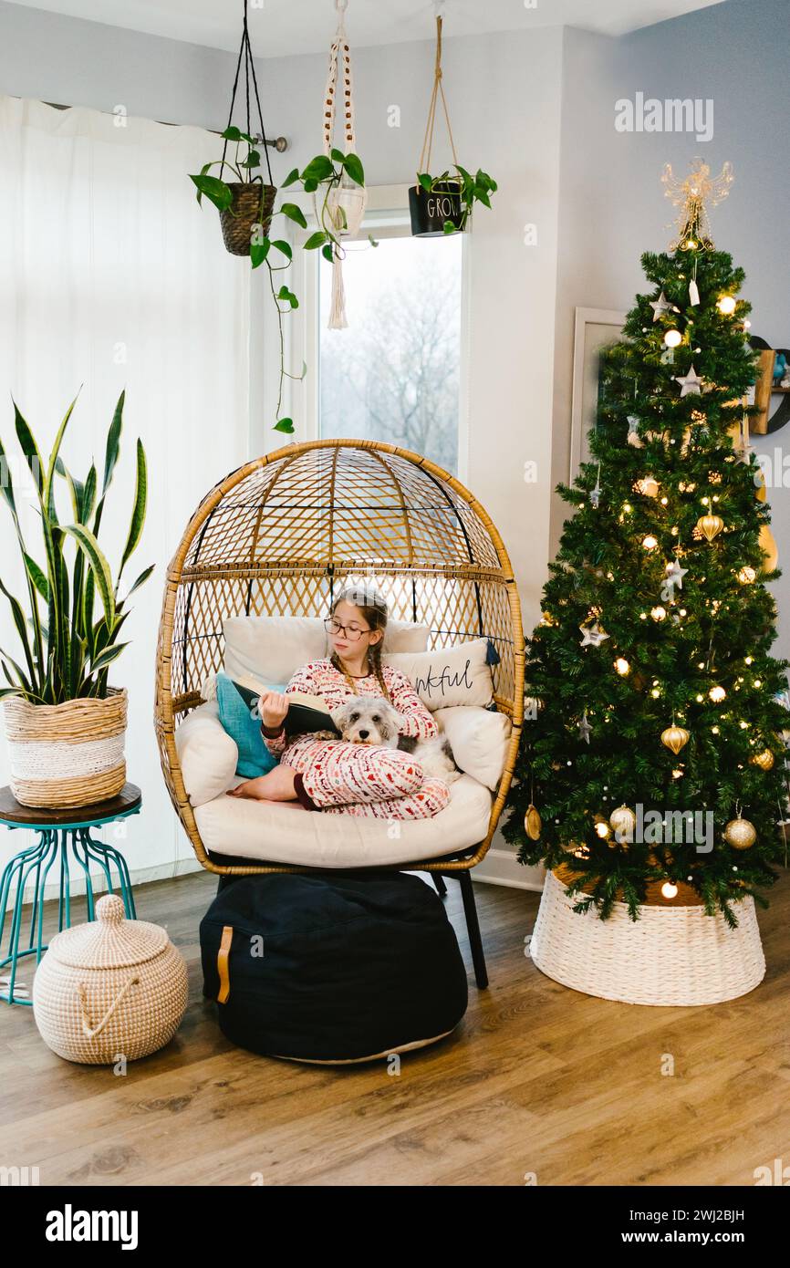 Tween fille dans le fauteuil d'oeuf à la maison se blottit avec chiot à Noël Banque D'Images