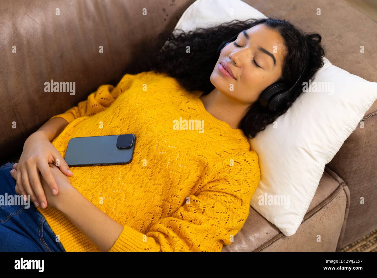 Femme biraciale avec casque et smartphone couché sur le canapé à la maison Banque D'Images