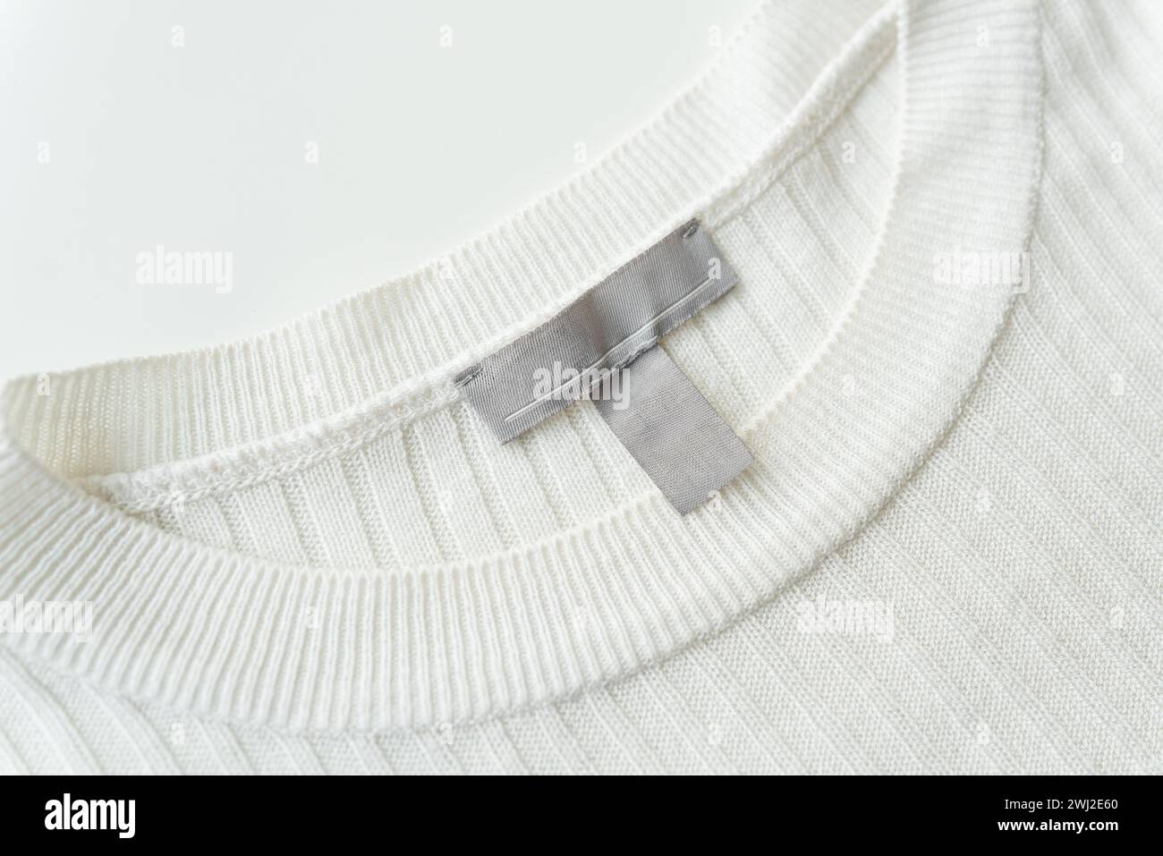 Gros plan d'un col de pull tricoté blanc avec une étiquette grise, soulignant la texture et la qualité du tissu Banque D'Images