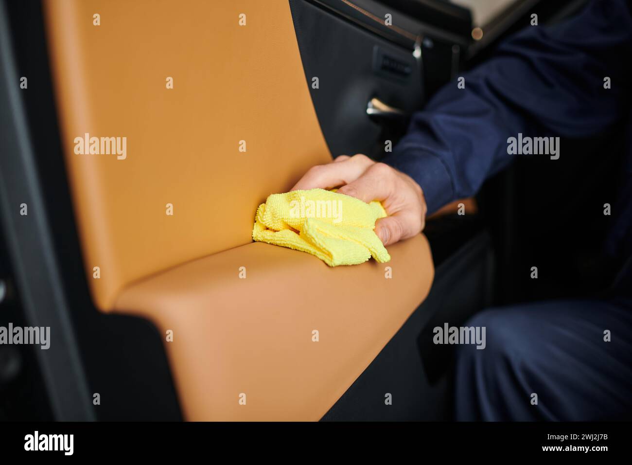 vue rognée d'un spécialiste dévoué travaillant dur dans la voiture de nettoyage uniforme bleu avec chiffon jaune Banque D'Images