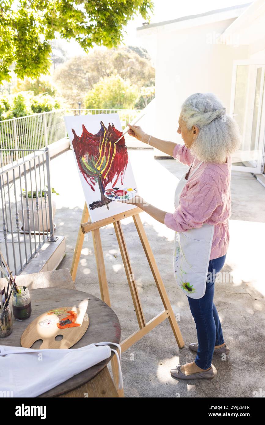 Femme senior caucasienne peignant sur toile sur terrasse ensoleillée Banque D'Images