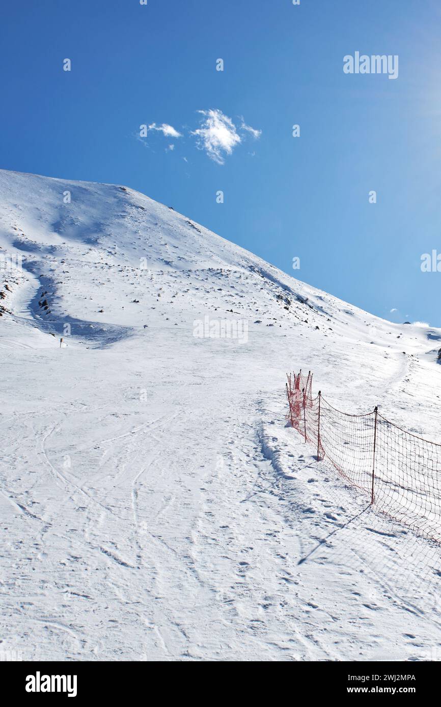Paysage de montagnes d'hiver à la journée ensoleillée. Piste vide à la station de ski, pente de montagne. Clôture en maille rouge marquant la zone dangereuse et la bordure du RO Banque D'Images