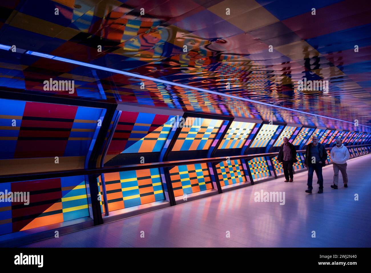 Des personnes interagissant avec l’œuvre d’art contemporain publique géométrique captivée par Colour par l’artiste Camille Walala dans la passerelle du tunnel à Adams Plaza Bridge reliant North Collonade à Crossrail place au cœur du quartier financier de Canary Wharf le 6 février 2024 à Londres, Royaume-Uni. Canary Wharf est une zone située près de l'île des chiens dans le quartier londonien de Tower Hamlets et est définie par la Greater London Authority comme faisant partie du quartier central des affaires de Londres. Banque D'Images