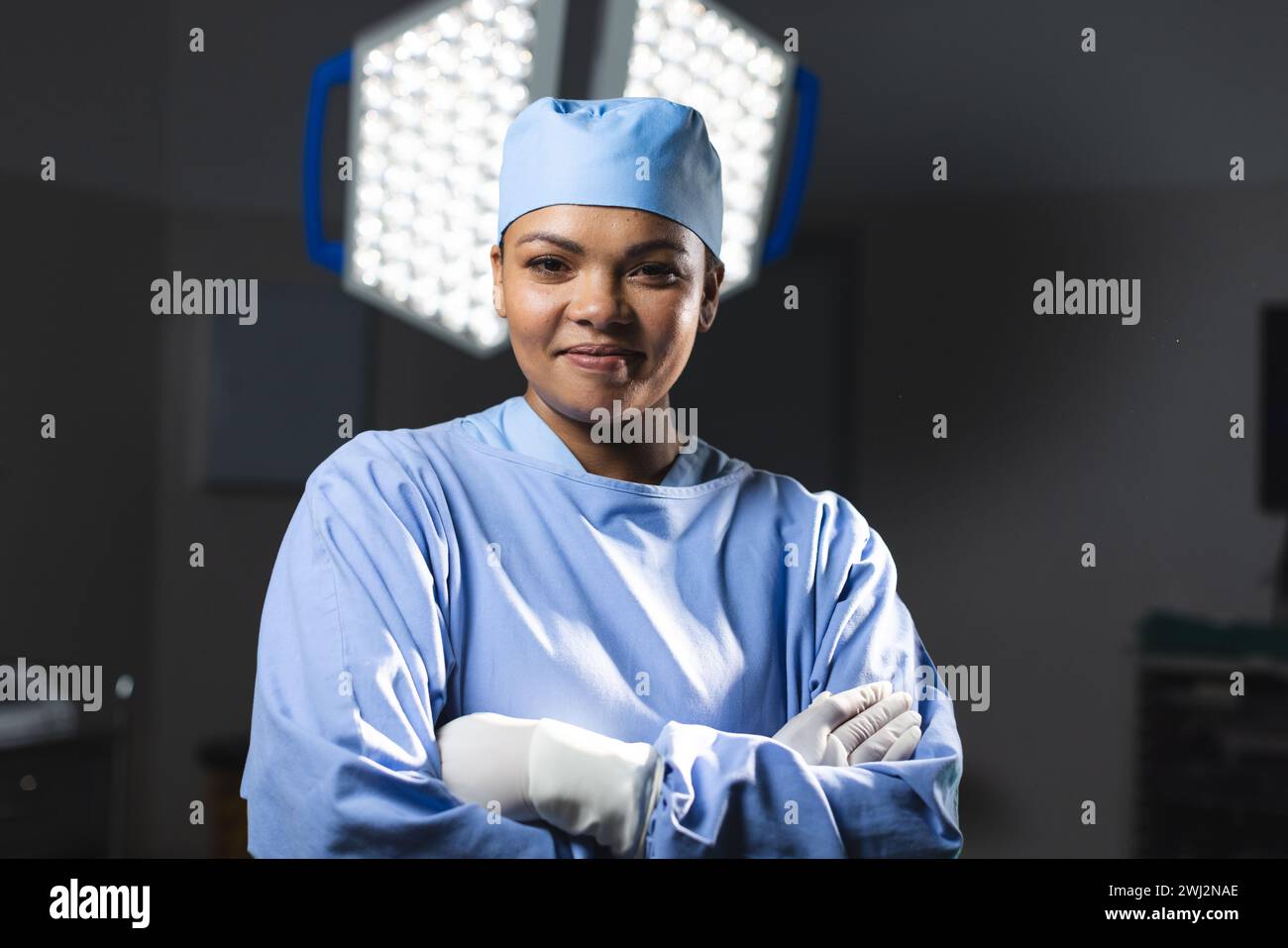 Portrait d'une chirurgienne biraciale heureuse portant une robe chirurgicale en salle d'opération Banque D'Images