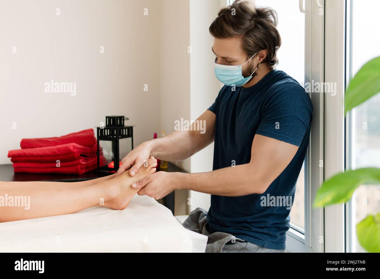 Masseur homme professionnel portant un masque de prévention pendant le massage des pieds féminin Banque D'Images