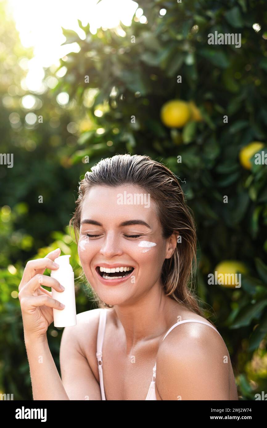 Femme joyeuse et belle appliquant une crème hydratante ou un écran solaire sur sa peau du visage Banque D'Images