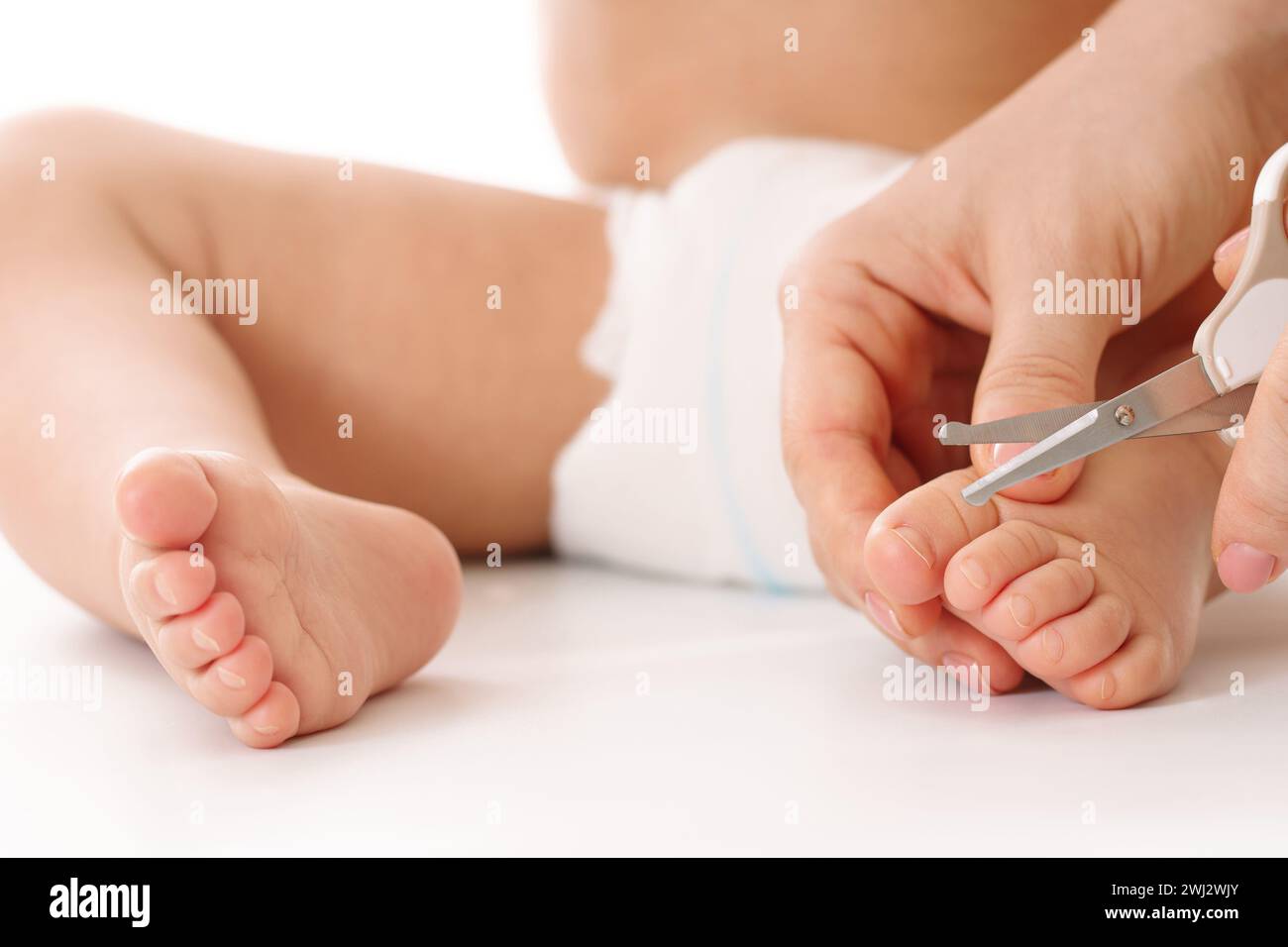 Mère tenant le pied du petit enfant et coupant les ongles des orteils. Banque D'Images