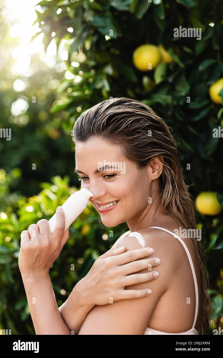 Femme joyeuse et belle appliquant une crème hydratante ou un écran solaire sur son corps Banque D'Images