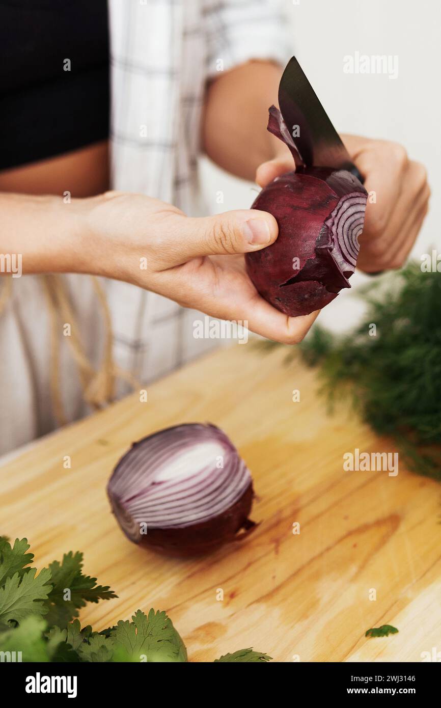 Mains féminines avec couteau épluchant l'oignon rouge pendant la cuisson Banque D'Images