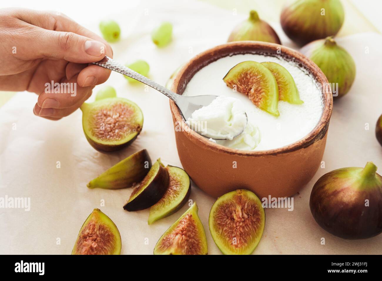 Cuillère et délicieux yogourt grec naturel dans un bol en argile avec des figues Banque D'Images