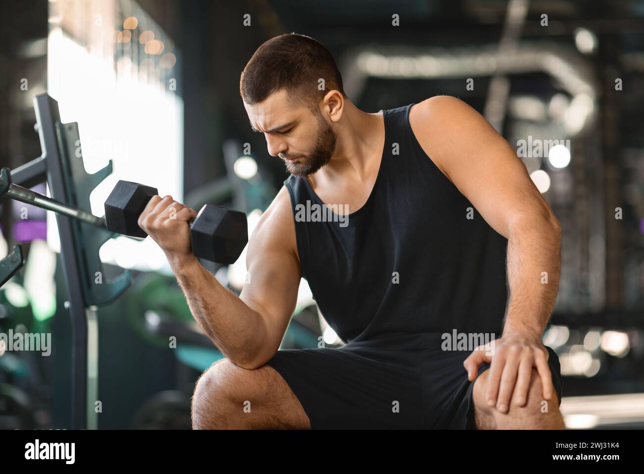 Athlète masculin barbu faisant un exercice de flexion des biceps assis au gymnase Banque D'Images