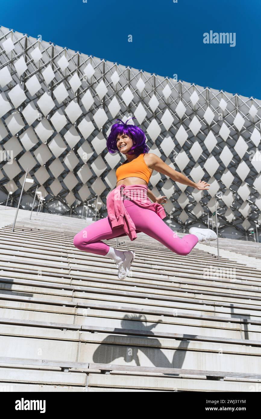 Femme insouciante portant des vêtements de sport colorés sautant dans la rue pendant la journée d'été Banque D'Images