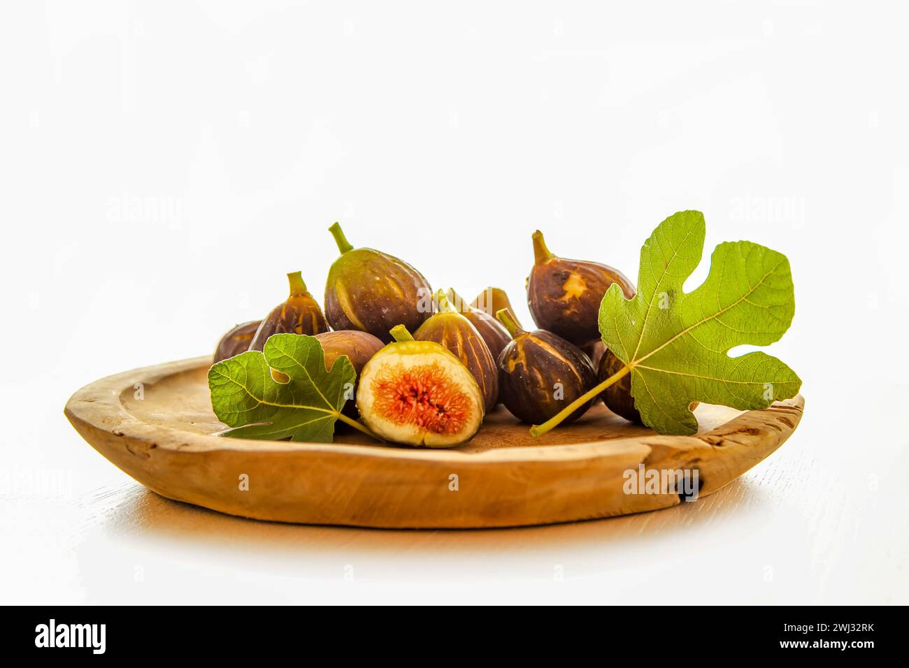 Figues crues fraîches et et coupées portion et feuille de vigne sur une table, sur une assiette en bois isolé Banque D'Images