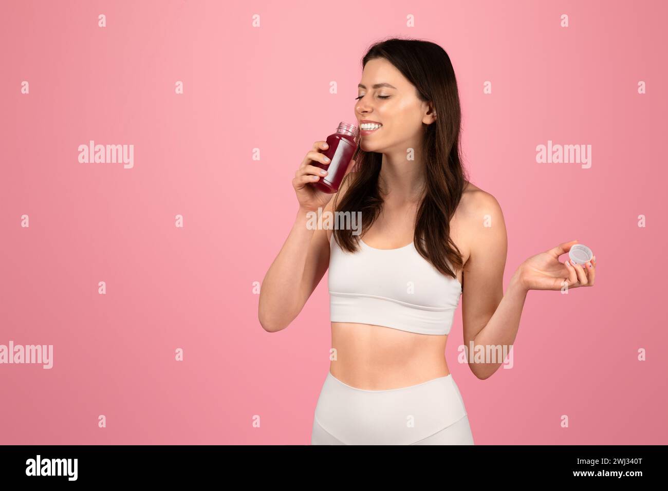 Une femme soucieuse de sa santé en vêtements de sport blancs apprécie un jus de betterave frais tout en tenant un bouchon de bouteille Banque D'Images