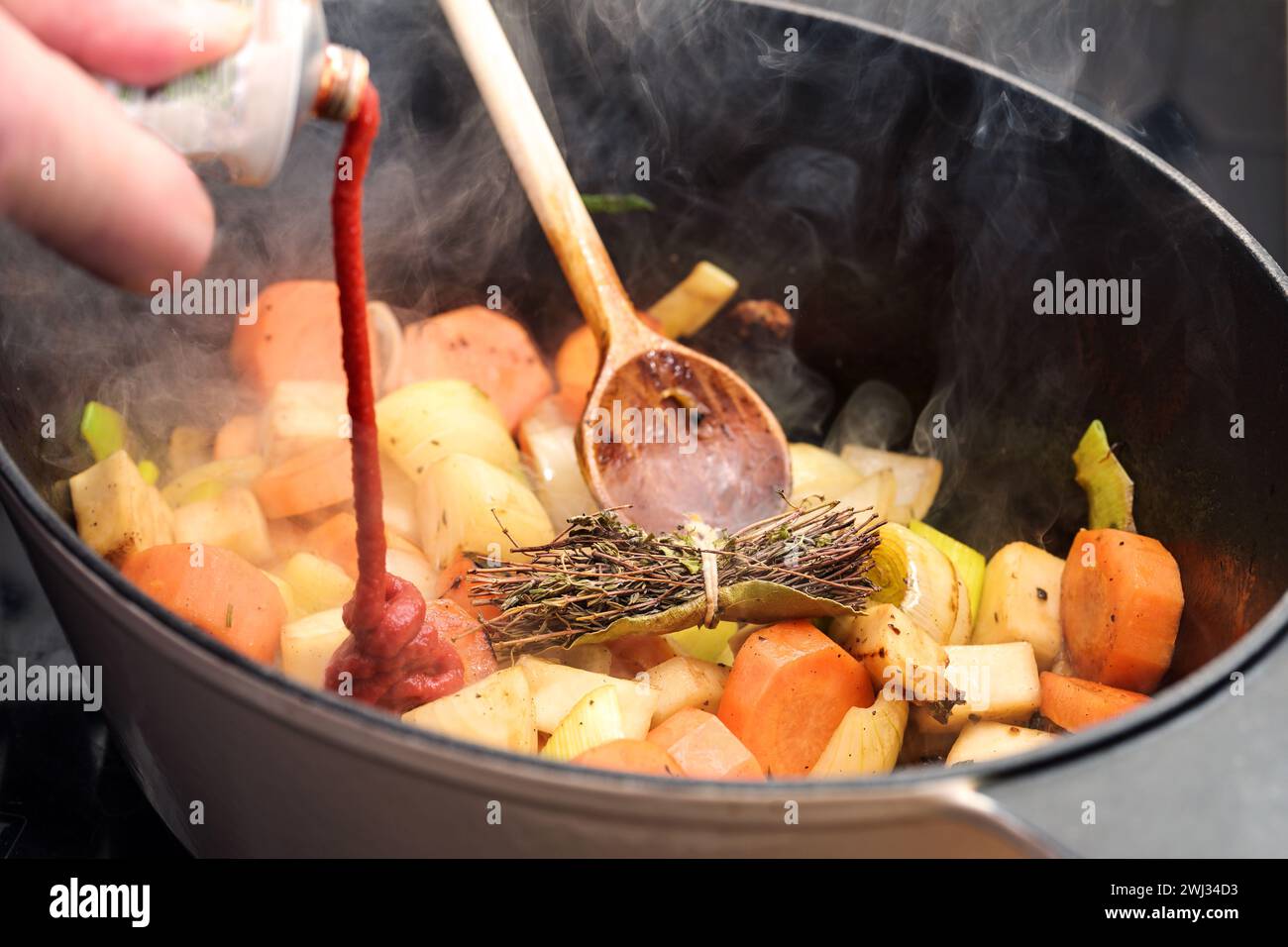 La pâte de tomate est versée dans une casserole avec des légumes rôtis à la vapeur comme la carotte, l'oignon, le céleri, le poireau et un bouquet d'herbes Banque D'Images