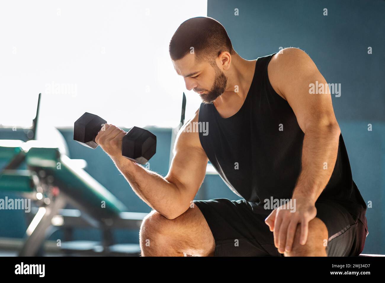 Jeune athlète masculin entraînement avec Dumbbell au gymnase, faisant des biceps assis Curl Banque D'Images