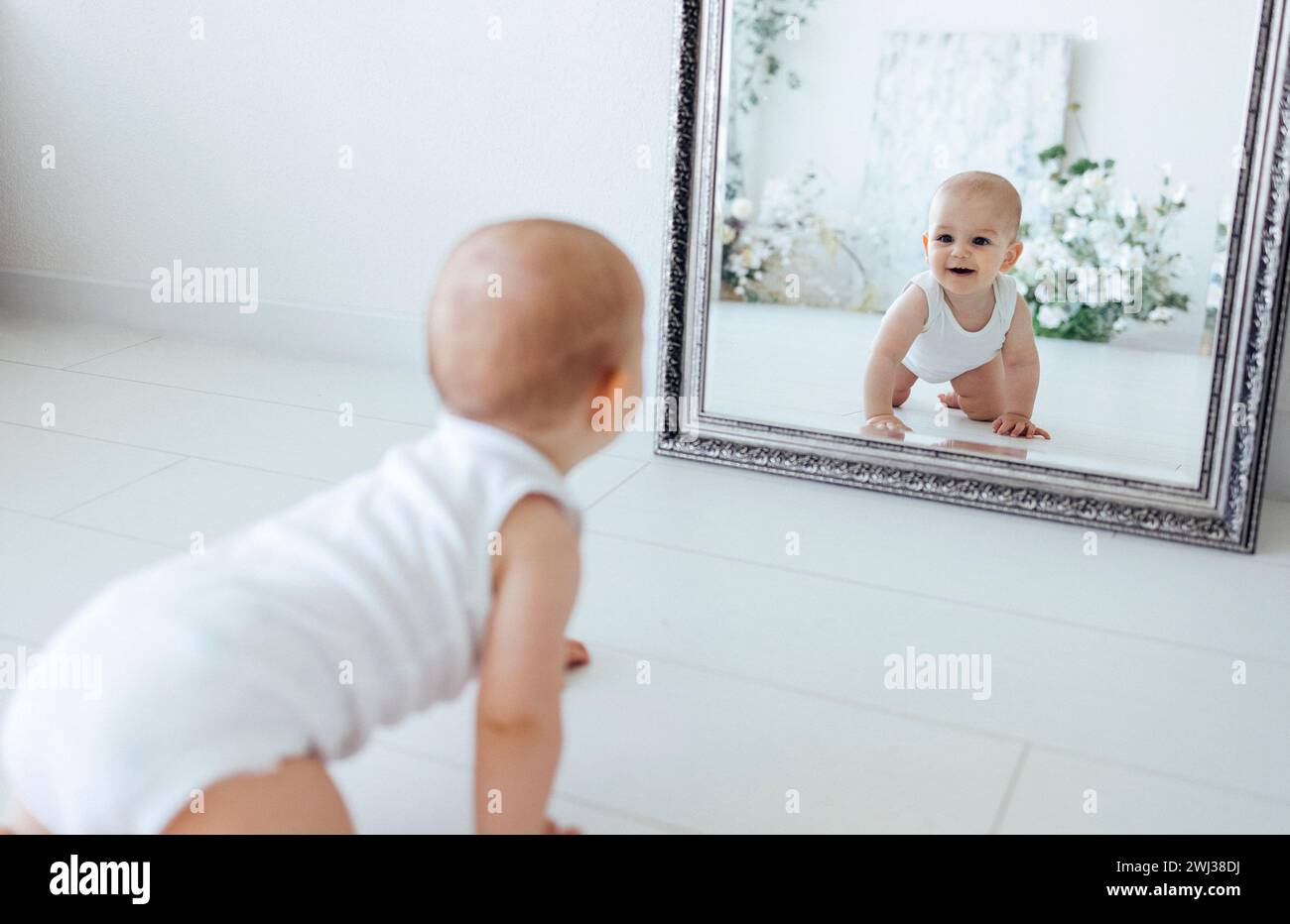Sweet Baby en bodyswuit blanc rampant à travers le sol jusqu'au miroir. Banque D'Images