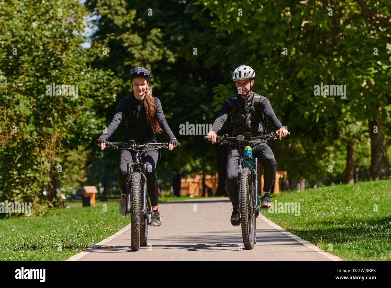 Un couple heureux, orné de matériel cycliste professionnel, profite d'une balade romantique à vélo à travers un parc, entouré de nat moderne Banque D'Images