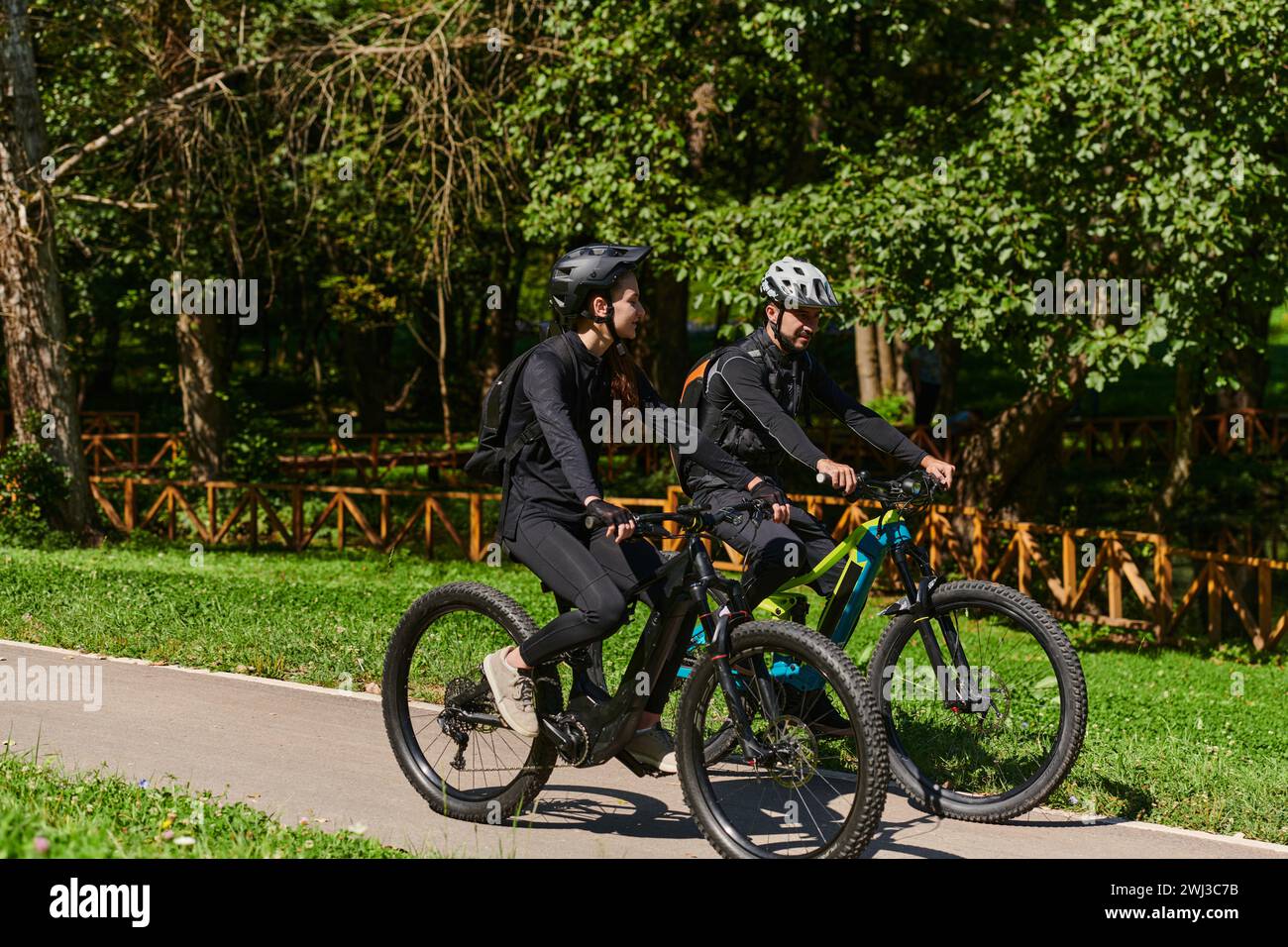Un couple heureux, orné de matériel cycliste professionnel, profite d'une balade romantique à vélo à travers un parc, entouré de nat moderne Banque D'Images