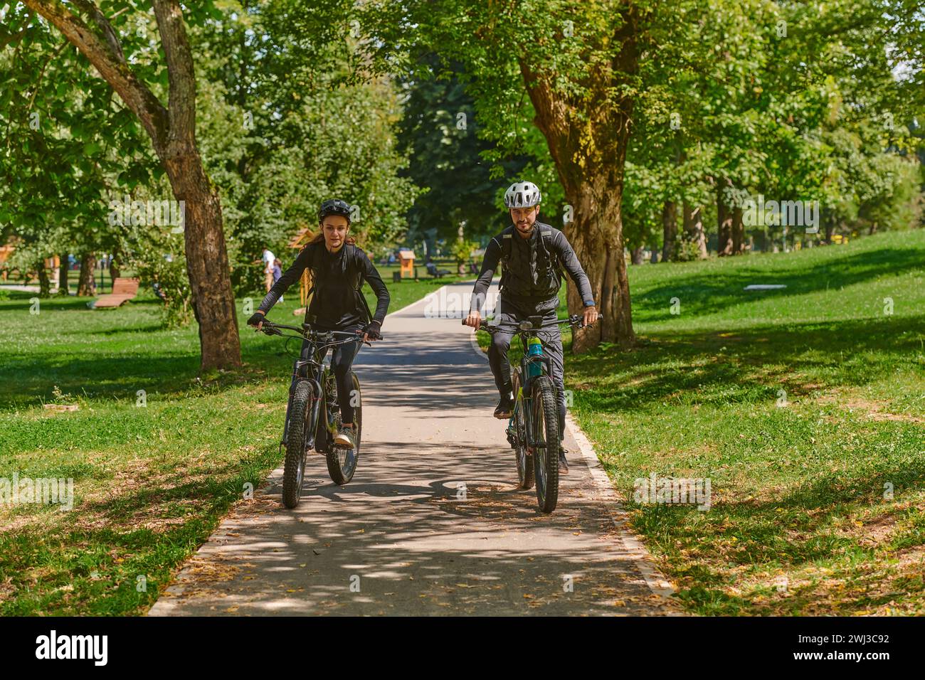 Un couple heureux, orné de matériel cycliste professionnel, profite d'une balade romantique à vélo à travers un parc, entouré de nat moderne Banque D'Images