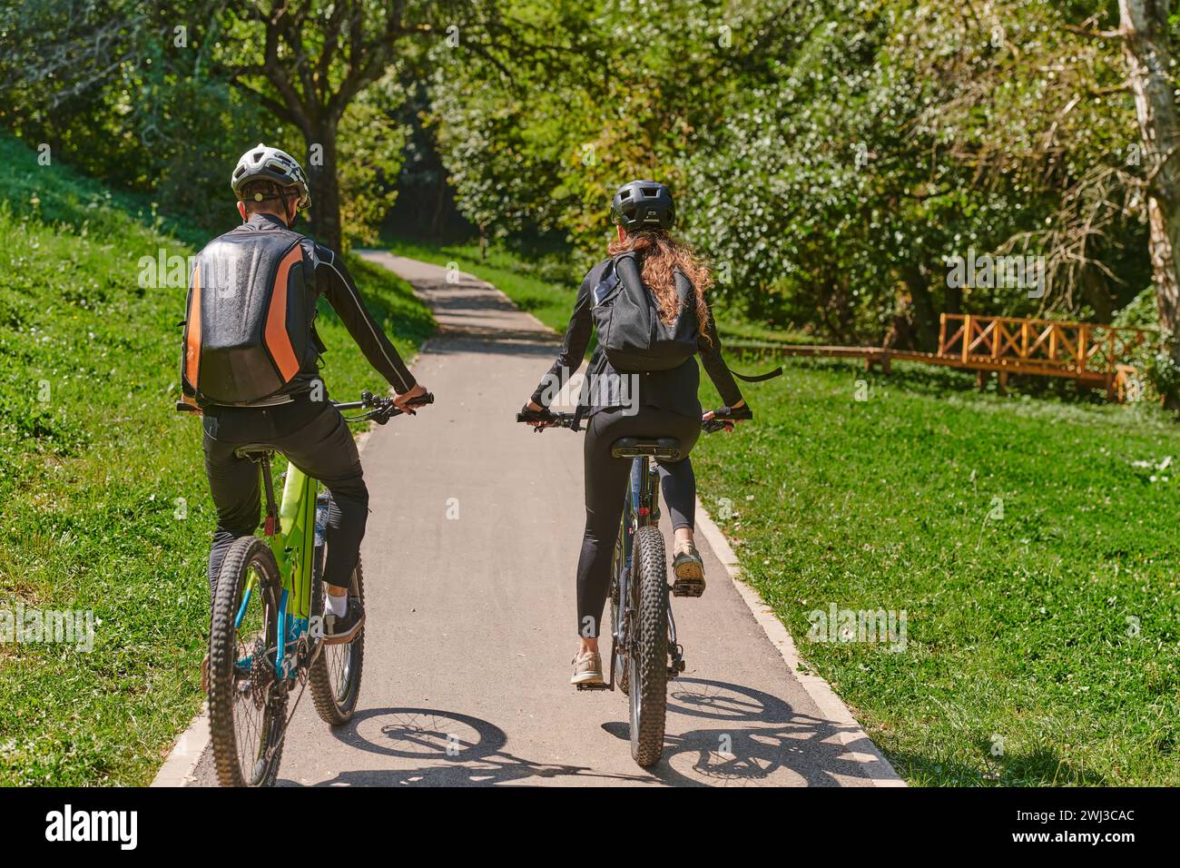 Un couple heureux, orné de matériel cycliste professionnel, profite d'une balade romantique à vélo à travers un parc, entouré de nat moderne Banque D'Images