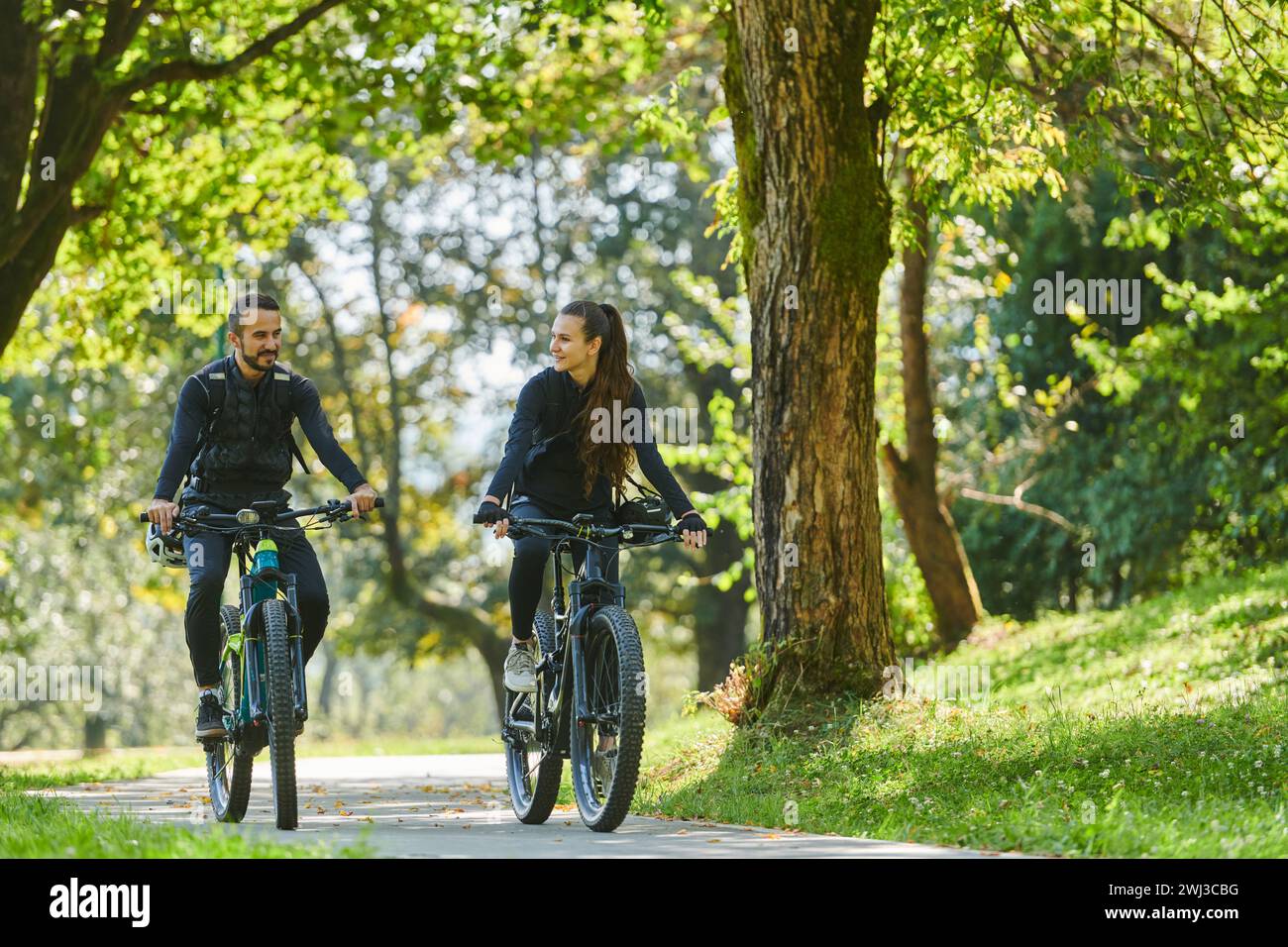 Un couple heureux, orné de matériel cycliste professionnel, profite d'une balade romantique à vélo à travers un parc, entouré de nat moderne Banque D'Images