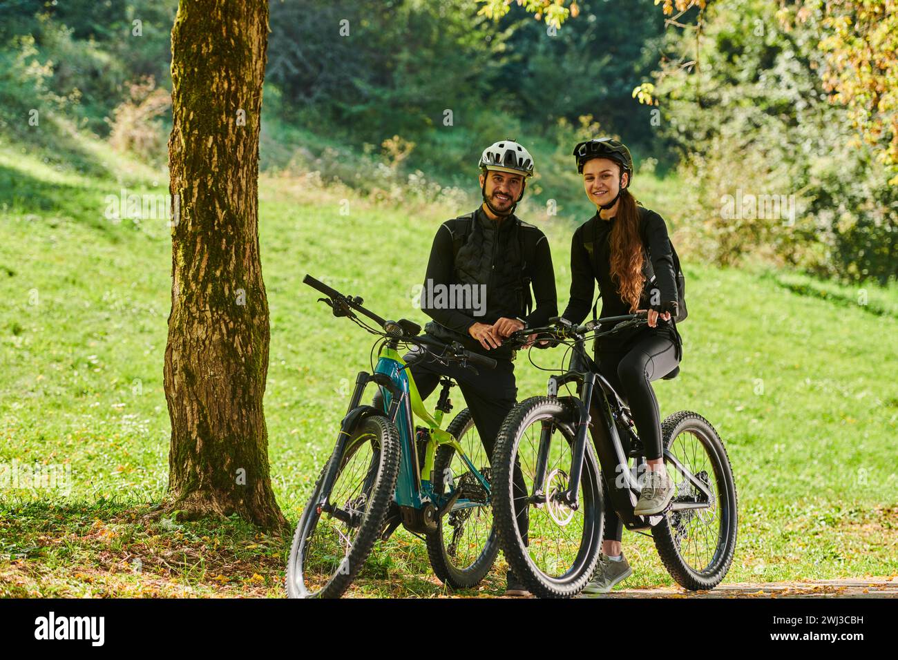 Un couple heureux, orné de matériel cycliste professionnel, profite d'une balade romantique à vélo à travers un parc, entouré de nat moderne Banque D'Images