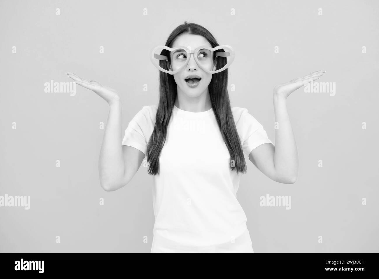 Beauté drôle adolescente fille avec des verres de fête, fond jaune. Surprise jeune femme avec des lunettes en forme de coeur. Banque D'Images