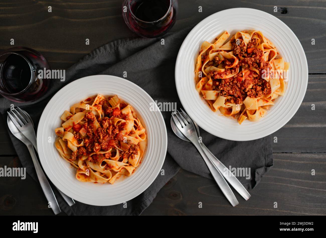 Bols de nouilles Pappardelle servis dans une sauce bolognaise authentique : bols de nouilles peu profonds vus directement d'en haut avec du vin et de l'argenterie Banque D'Images