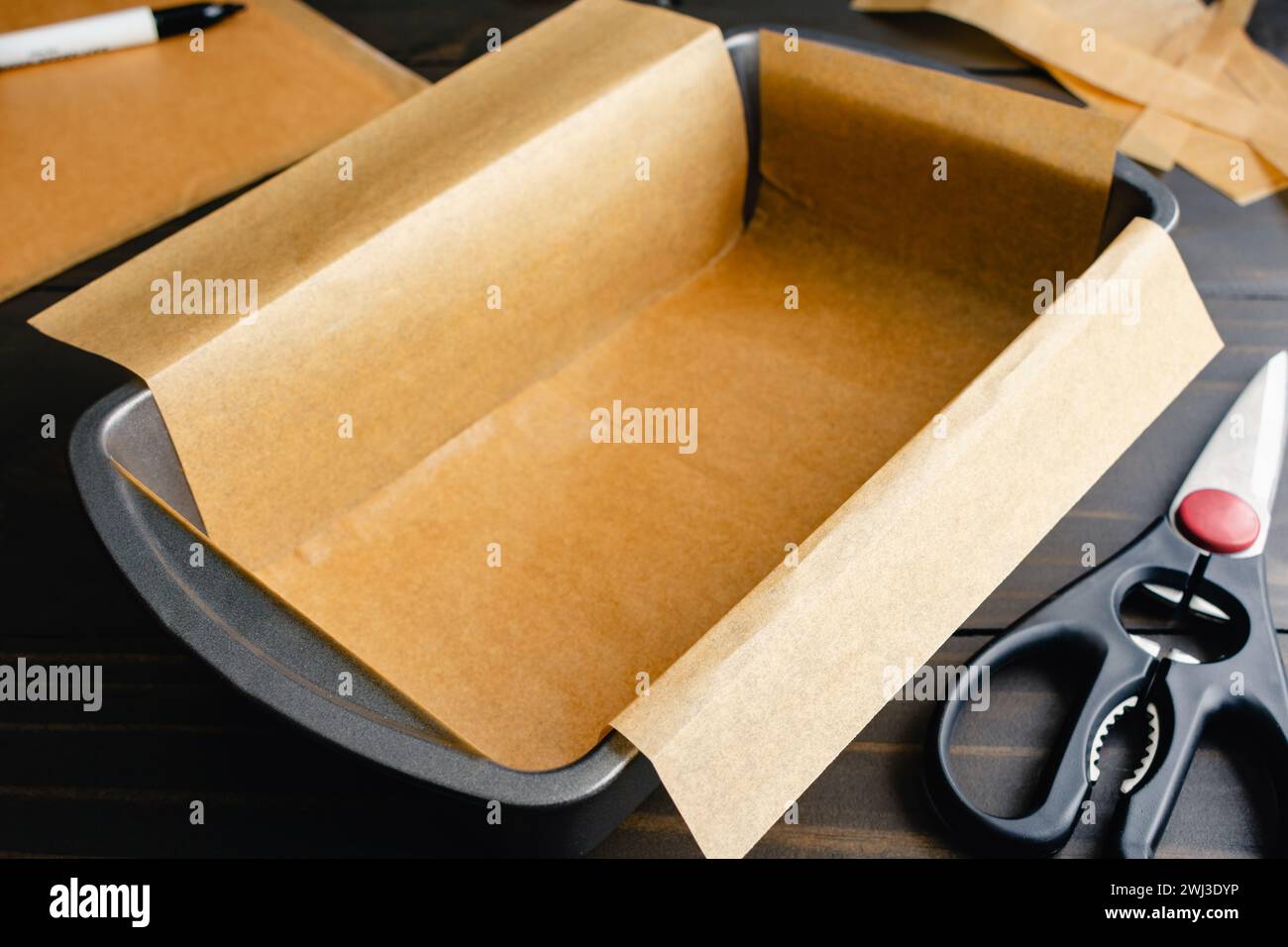Moule à pain garni de papier parchemin non blanchi : moule à pain garni de papier sulfurisé avec des ciseaux et un marqueur en arrière-plan Banque D'Images