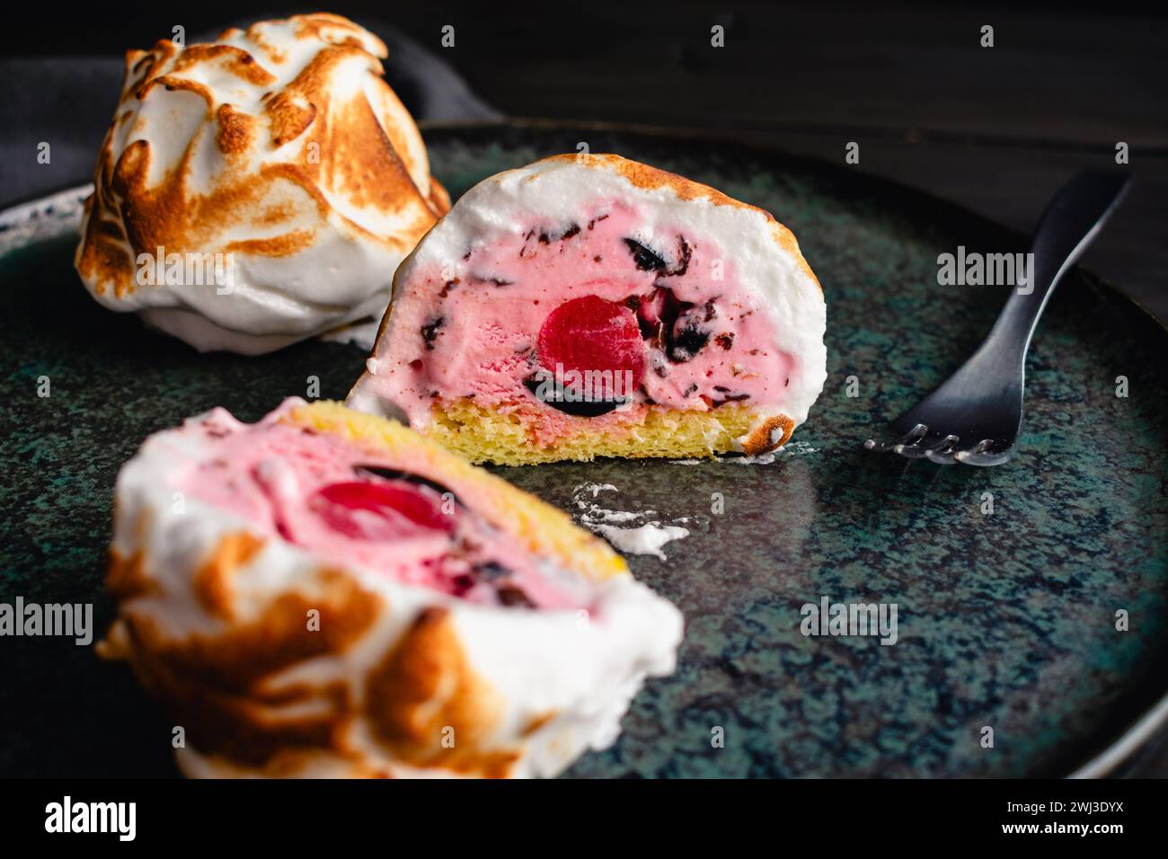 Tranchées Mini Baked Alaska avec un centre de cerises : boule de crème glacée rose avec des pépites de chocolat sur un gâteau éponge entouré de meringue torchée Banque D'Images