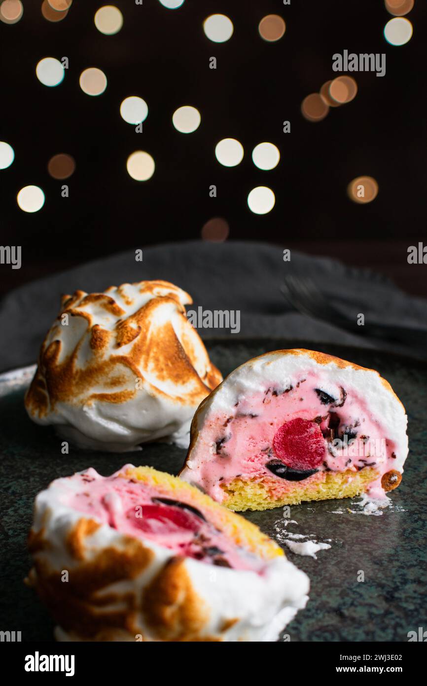 Tranchées Mini Baked Alaska avec un centre de cerises : boule de crème glacée rose avec des pépites de chocolat sur un gâteau éponge entouré de meringue torchée Banque D'Images