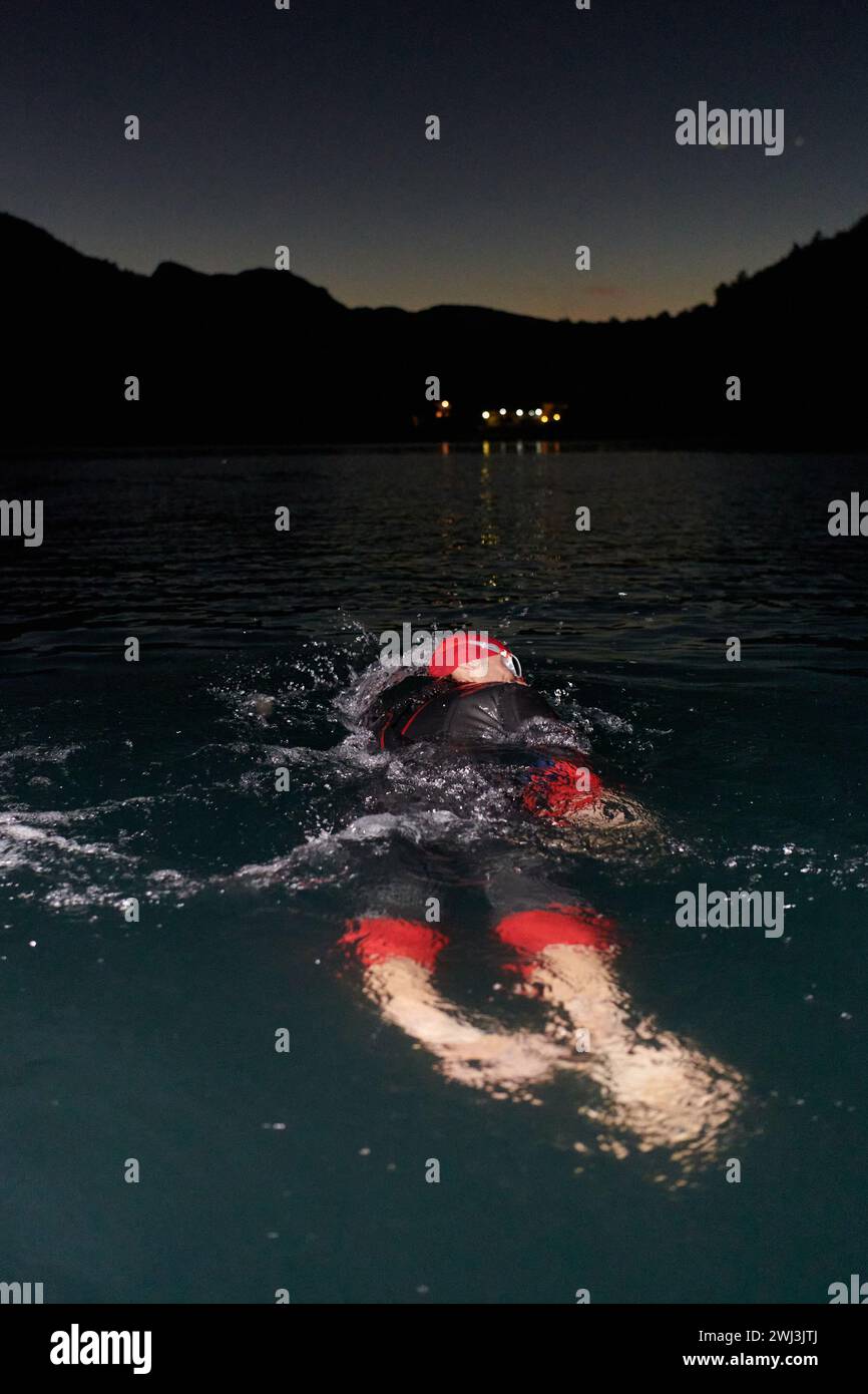 Un triathlète professionnel déterminé suit un entraînement nocturne rigoureux dans les eaux froides, mettant en valeur son dévouement et sa résilience Banque D'Images