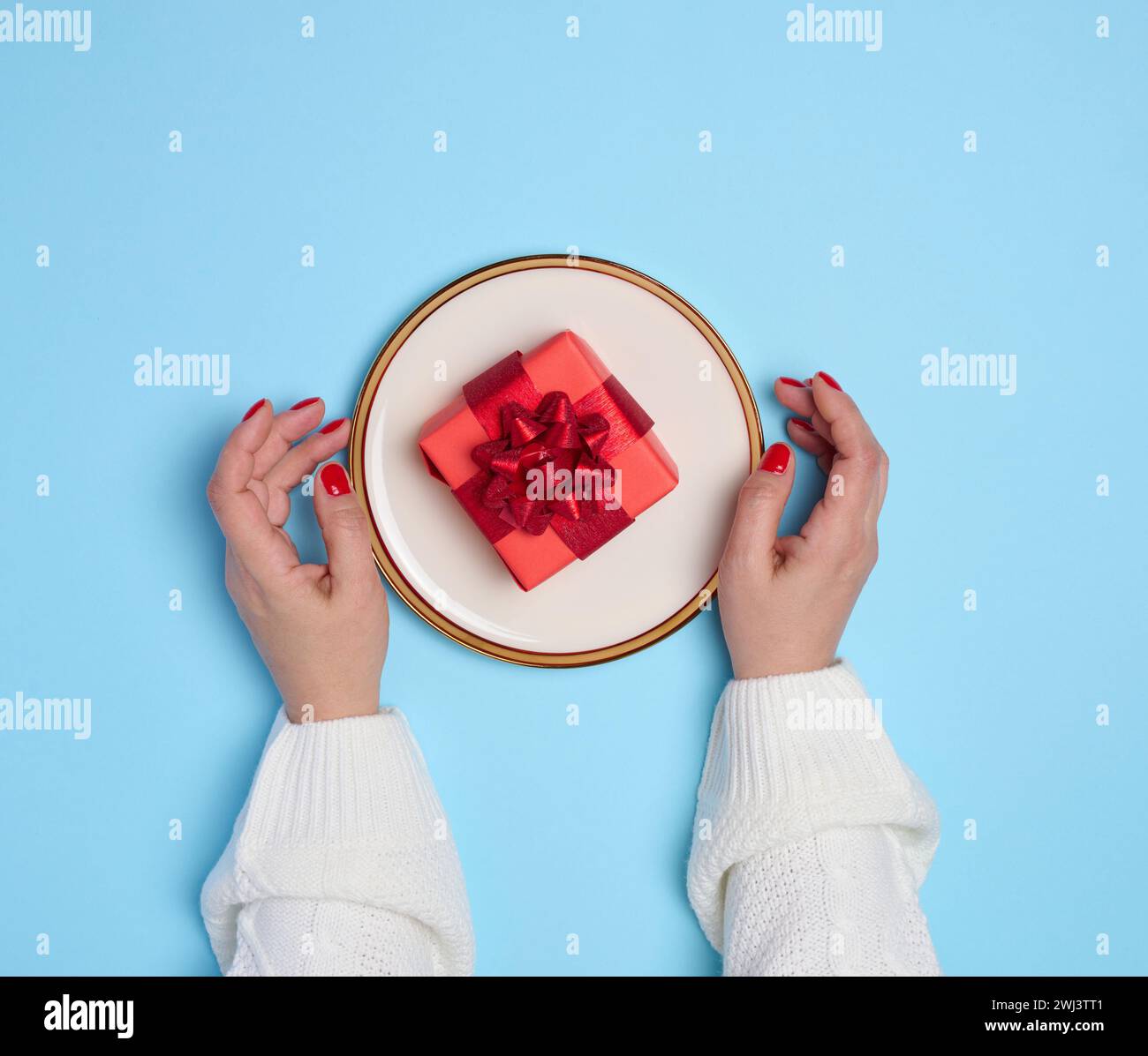 Deux mains féminines tenant une assiette avec un cadeau sur fond bleu Banque D'Images