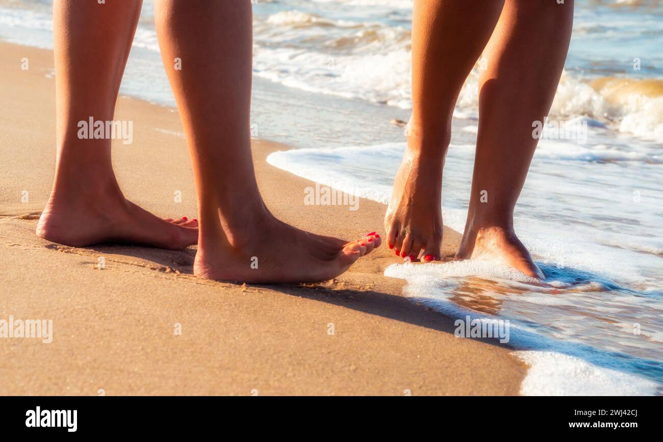 Pieds féminins sur une plage de sable dans les vagues du surf de la mer en été près Banque D'Images