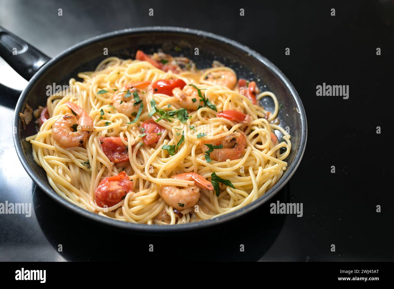 Spaghetti aux crevettes, tomates et herbes une poêle noire sur le dessus de la cuisinière, la cuisson d'un repas de fruits de mer méditerranéens, espace copie Banque D'Images