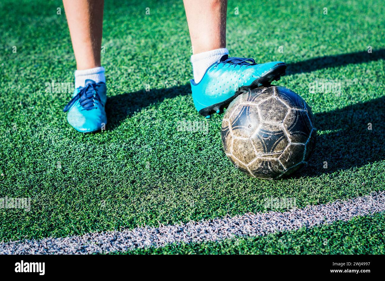 Jambes d'un adolescent joueur de football de rue dans des chaussures de football bleues avec un ballon de football sur un terrain de football vert Banque D'Images