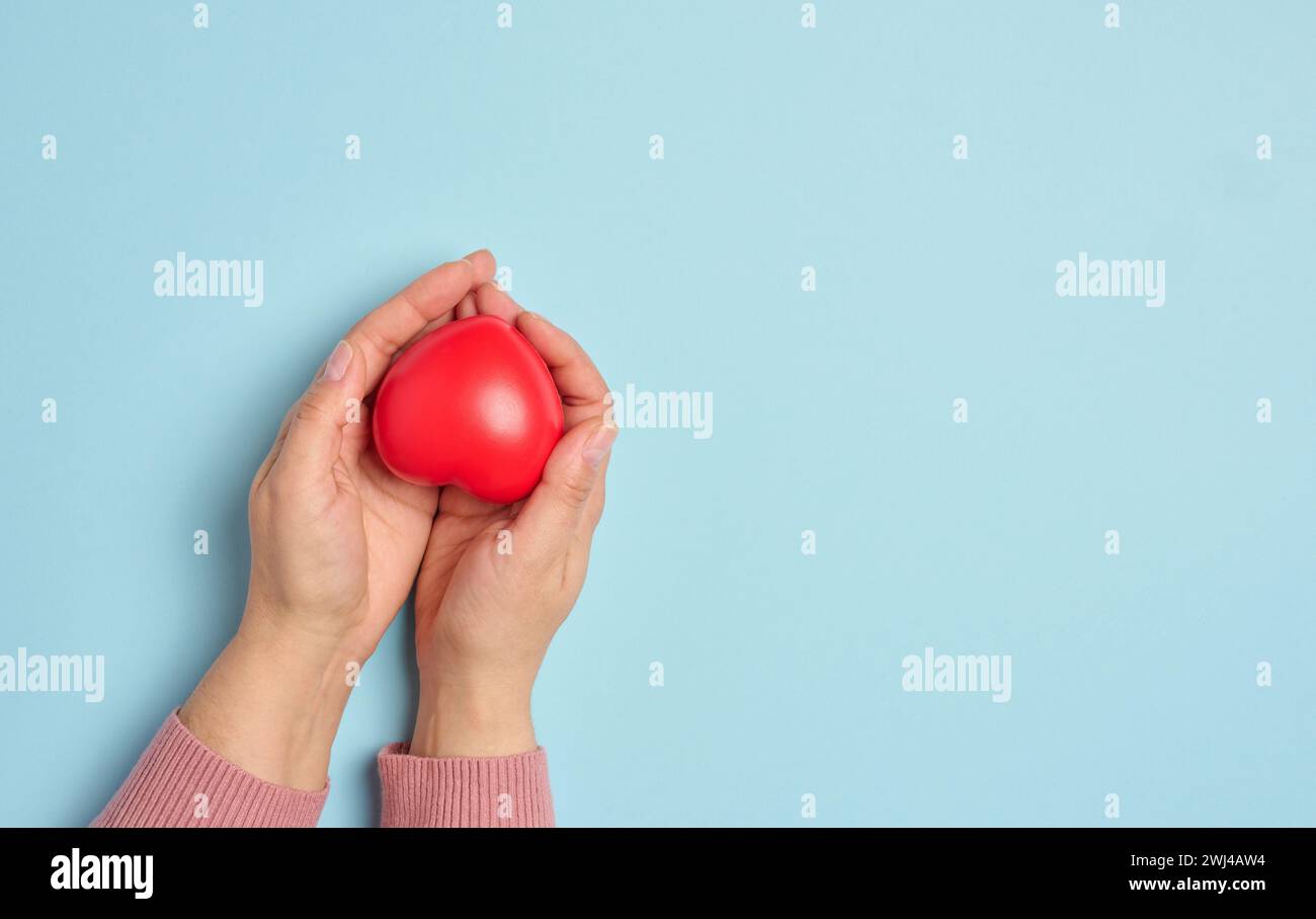 La main d'une femme tient un cœur en caoutchouc rouge sur fond bleu, symbolisant le concept de don Banque D'Images