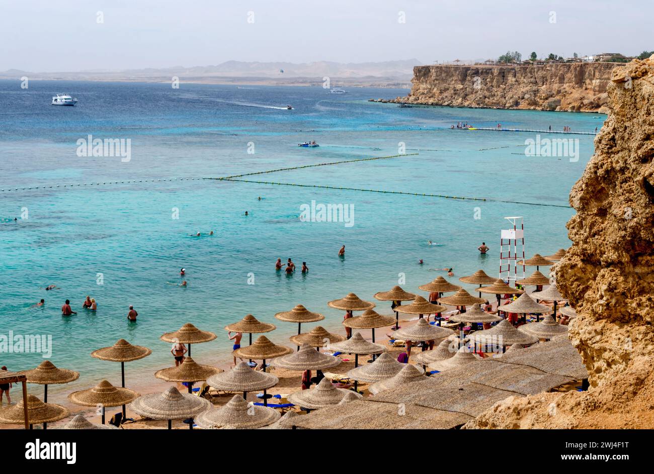 Vue du haut de la plage avec des parasols de bateaux de roseaux et des gens debout dans l'eau bleue Banque D'Images Vue du haut de la plage avec des parasols de bateaux de roseaux et des gens debout dans l'eau bleue Banque D'Images