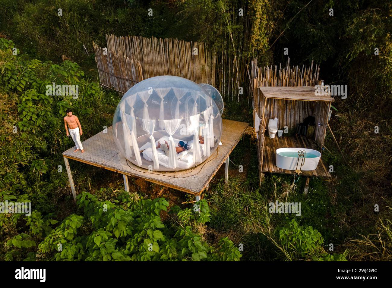 Couple homme et femmes dans une tente à bulles avec une salle de bain extérieure avec baignoire dans la forêt tropicale de la jungle Banque D'Images