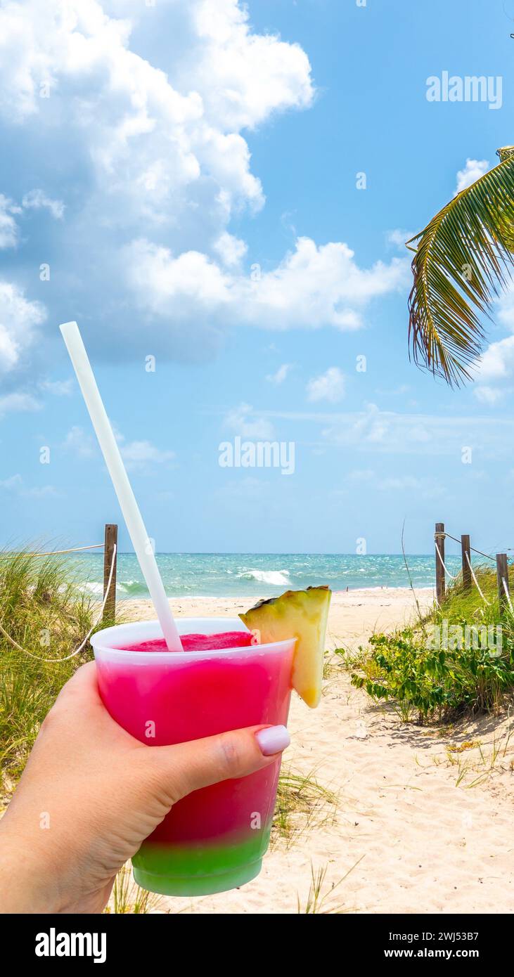 Main tenant un verre avec un cocktail et de la paille et Sand Path allant à l'océan à Miami Beach, Floride Banque D'Images