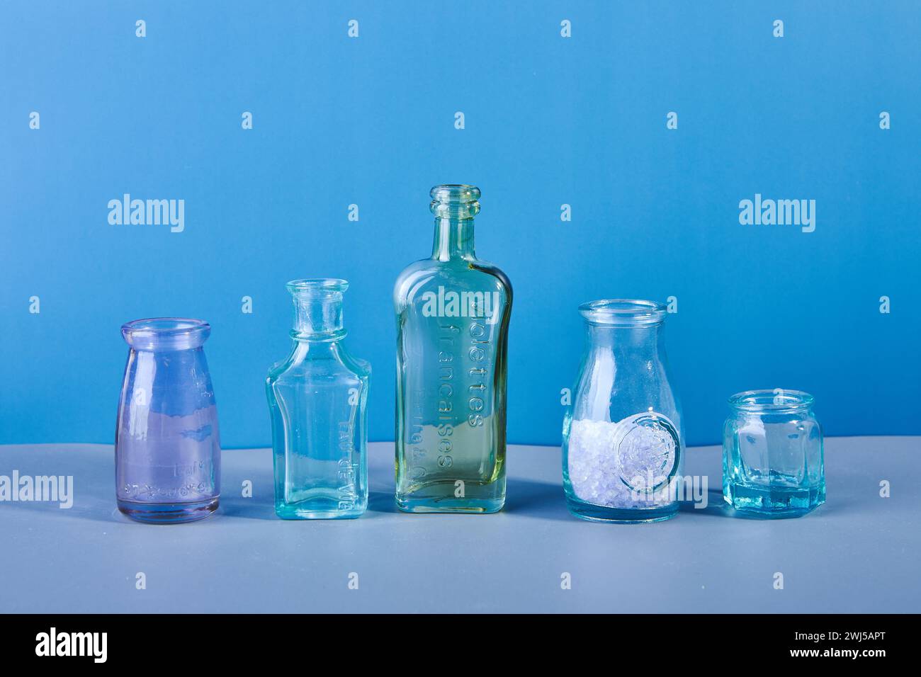 Ensemble de diverses bouteilles et vases en verre et en métal colorés sourds sur un fond bleu. Banque D'Images