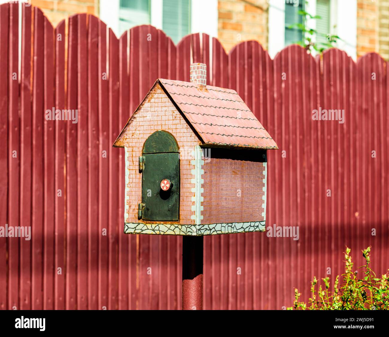 Boîte aux lettres sous la forme d'une petite maison sur le fond d'une clôture rouge Banque D'Images
